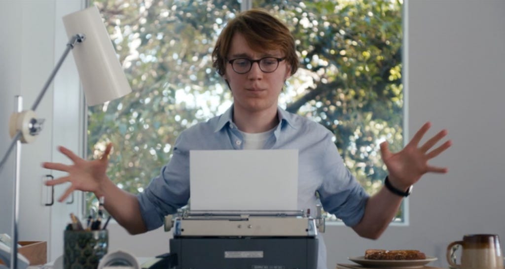 a man sitting in front of a loaded typewriter looking very serious, waving hands in the air