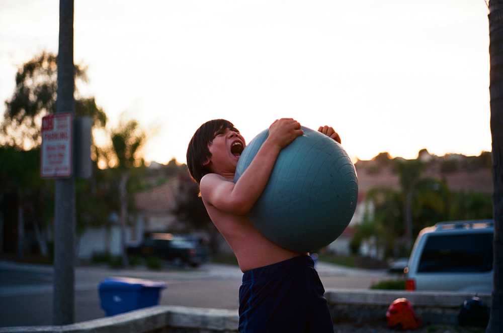 shirtless boy hugging a ball trying to squash it