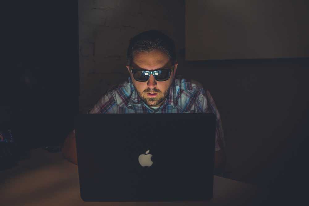 guy wearing shades working on laptop in a dark room